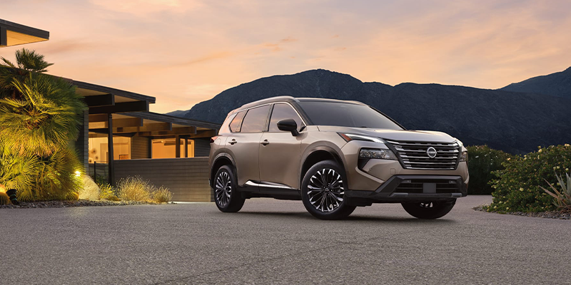 A silver Nissan Rogue parked in front of a house at sunset with a mountain view.