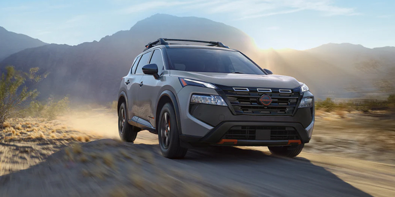 A silver Nissan Rogue driving on a dirt road.