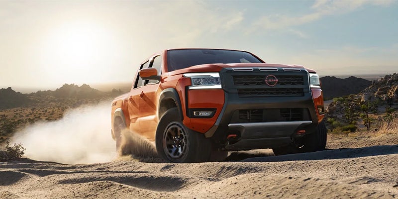 A vibrant orange Nissan Frontier PRO-4X midsize pickup truck kicking up dust in an off-road desert setting.